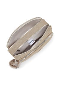 Beige zippered pouch with a textured exterior, multiple compartments, silver hardware, and a fluffy pom-pom accent on the zipper pull.