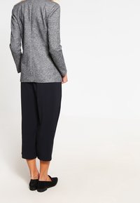 Blazer gris texturé à coupe ajustée, associé à un pantalon noir ample et court ainsi qu'à des chaussures noires sans lacets. Design simple et moderne.