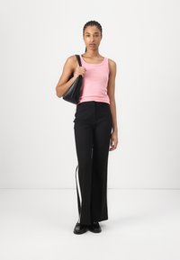 Haut sans manches rose avec un col rond, associé à un pantalon noir taille haute avec des rayures latérales et des chaussures noires.