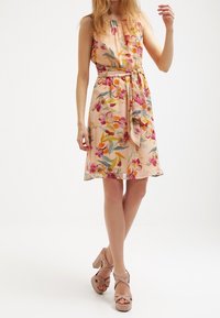 Robe sans manches florale en tissu pêche doux, dotée d'une taille ceinturée, avec des fleurs multicolores et des feuilles vertes sur l'ensemble du design.