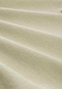 Teksturowana, jasnozielona tkanina z delikatnym wzorem siatki, ukazująca falowania i zagięcia, które sugerują wagę i miękkość.