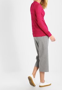Roze gebreide trui met een gestructureerd patroon, gecombineerd met lichtgrijze cropped broek en witte sneakers met een bruine zool.