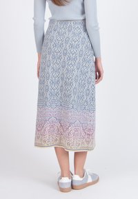 Kvinde iført en mønstret midi-nederdel med blå, pink og gule designs, en lyseblå ribbet langærmet top og grå og hvide sneakers.