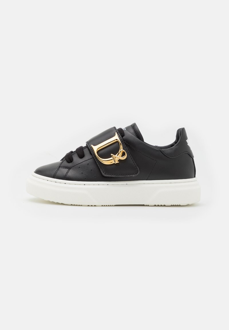 Sneaker in pelle nera con suola bianca, chiusura con lacci e un dettaglio in metallo dorato sul lato. Texture liscia con accenti perforati.