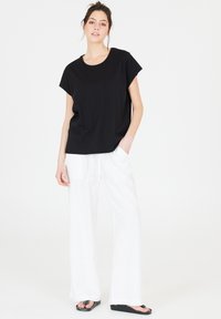 Black t-shirt with short sleeves and a rounded neckline, paired with loose, white, high-waisted pants and black, flat sandals.