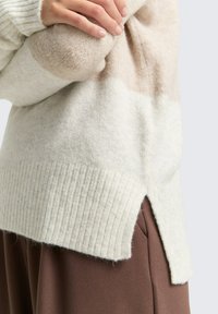 Maglione a maglia beige chiaro con orlo a coste e spacchi laterali, caratterizzato da una consistenza morbida e da un design a blocchi di colore nelle tonalità di crema e marrone chiaro.