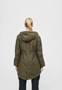 Olive green parka with a hood, elastic waist, and curved hem. Features buttoned back vent and smooth texture. Simple, functional design.