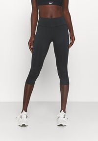 Black capri leggings with a high waistband, smooth texture, and subtle seam details, paired with white athletic shoes.