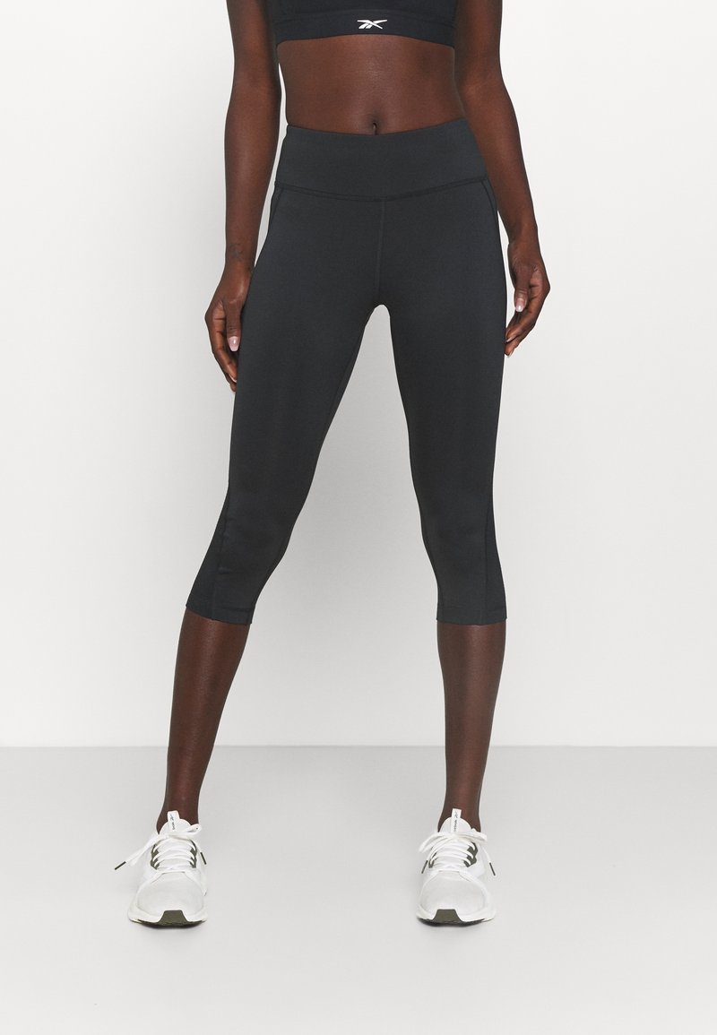 Black capri leggings with a high waistband, smooth texture, and subtle seam details, paired with white athletic shoes.