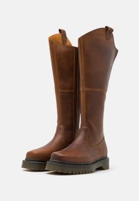 Brown leather knee-high boots with a zip closure, sturdy sole, and textured finish; features a low heel and contrasting stitching details.