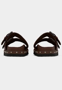 Καφέ σανδάλια με διπλές ρυθμιζόμενες λουρίδες, διακοσμητικά καρφιά κατά μήκος της σόλας και φαρδιά, διαμορφωμένη πάτημα. Υλικό με υφή και ματ φινίρισμα.