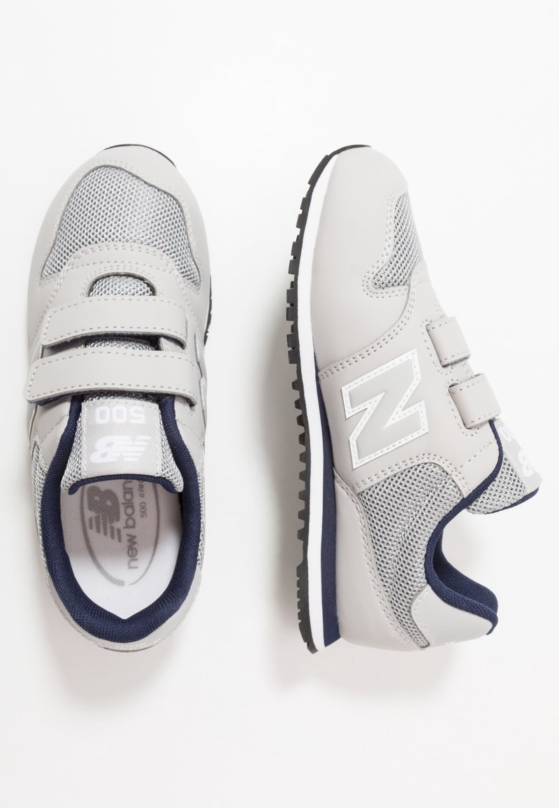 Grå sportskor med meshpaneler, kardborreband och marinblå detaljer. Har en vit logotyp och ett mönstrat gummisula för bra grepp.