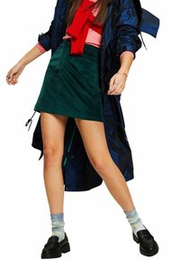 Groene corduroy minirok met een gladde textuur. Gecombineerd met een roze top en een rode sjaal, zwarte loafers en patroon sokken.