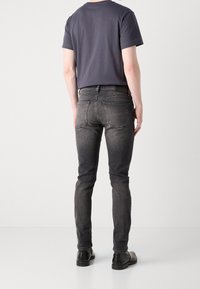 Tenké tmavě šedé džíny s hladkou texturou, pěti kapsami a kontrastním prošitím, zkombinované s jednobarevným tričkem s krátkým rukávem.