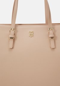 Beżowa torebka skórzana o fakturze, z dwiema regulowanymi ramiączkami na ramię i małym złotym logo Tommy Hilfiger umieszczonym centralnie z przodu.