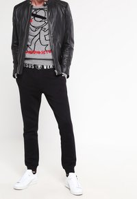 Zwarte leren jas over een grijze sweatshirt met grafisch ontwerp, gecombineerd met zwarte joggingbroeken en witte sneakers. Eenvoudige en moderne styling.