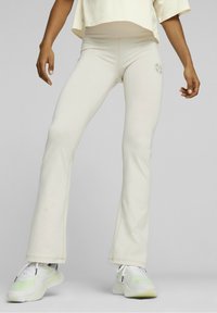 Leggings crème évasés en tissu extensible, dotés d'un petit logo près de la taille et de détails de couture contrastants.