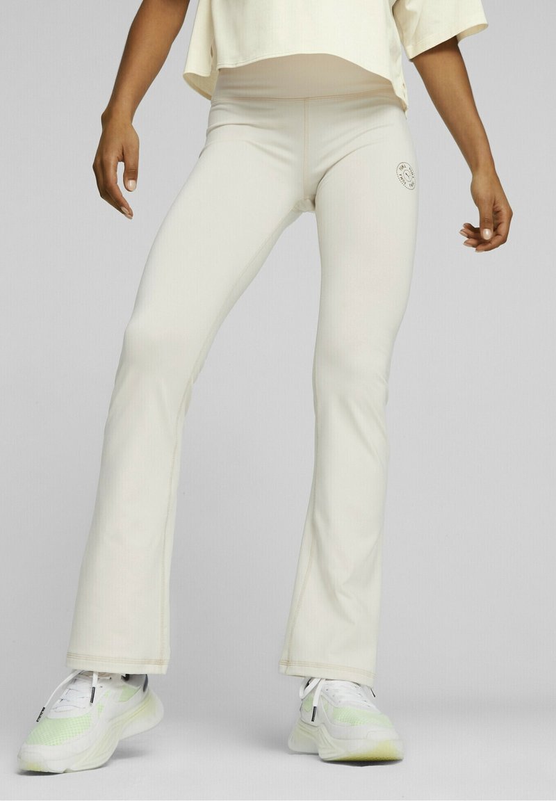 Leggings crème évasés en tissu extensible, dotés d'un petit logo près de la taille et de détails de couture contrastants.