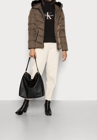 Brun puffjacka med pälsmössa, svart tröja med logotyp, krämfärgade byxor, svart läderväska samt klackade ankelskot. Minimalistisk design.