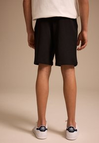 Black cotton shorts with an elastic waistband, featuring a straight cut. White sneakers with blue accents and logo detail on the heel.