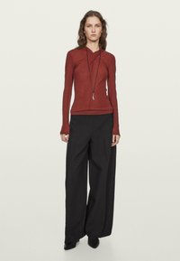 Červený top s dlouhým rukávem a přiléhavým střihem, s překříženým výstřihem. V kombinaci s černými širokými kalhotami s vysokým pasem a špičatými botami.