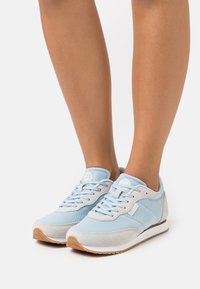 Ljusblå atletiska skor med mesh- och mockamaterial, snörningsdesign, gummisula och ett mönstrat inslag på hälen.