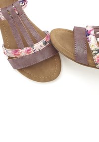 Purple sandals with floral accent straps, flat sole, and textured surfaces. The design features multiple straps across the foot and ankle.