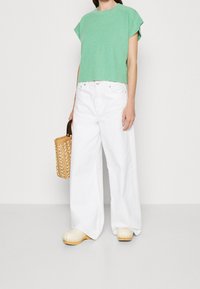 Zielony, króki dzianinowy top, białe szerokie dżinsy i jasne klapki. Dodatki to pleciona torebka z drewnianą rączką.