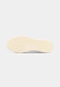 Kremo spalvos guminė sportinio batų pado dalis su tekstūruotu tinklo raštu ir apskrito akcento detalėmis, ant kulno įspaustas "Lacoste" logotipas.