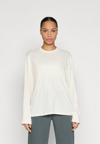 Long-sleeve cream top with a round neckline, made of soft fabric. Features subtle branding in light color on the chest.
