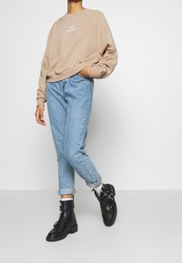Sweat-shirt beige avec texte blanc, jean bleu clair et bottines noires avec boucles argentées et semelles texturées. Présentation d'une tenue décontractée.