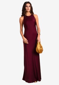 Abito lungo senza maniche bordeaux, dal design elegante e aderente, abbinato a una pochette dorata con lacci. Tessuto liscio con dettagli minimi.