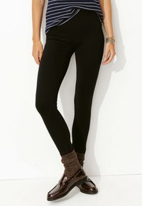 Leggings noirs avec une texture lisse et extensible, associés à des chaussures marron et des chaussettes métalliques brunes texturées. Le design est ajusté.
