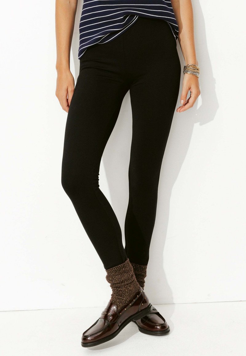 Leggings noirs avec une texture lisse et extensible, associés à des chaussures marron et des chaussettes métalliques brunes texturées. Le design est ajusté.