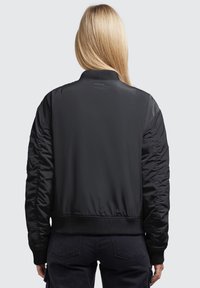Svart bomberjacka med texturerade, vadderade ärmar, ribbad krage och muddar samt en slät yta. Enkel design utan synliga logotyper.
