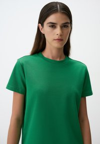 Zielona bawełniana koszulka z krótkimi rękawami, okrągłym dekoltem i gładką fakturą. Brak widocznych wzorów lub akcentów. Prosty, casualowy design.