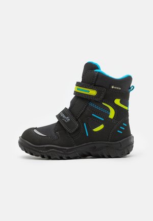 Sort vinterstøvle til børn med blå og gule accenter, dobbelte velcrolukninger, robust sål og vandtæt Gore-Tex-materiale.