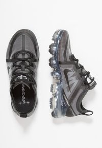 Scarpe da ginnastica atletiche nere e grigie in rete con suole traslucide, superficie testurizzata, sistema di allacciatura distintivo e battistrada in gomma.