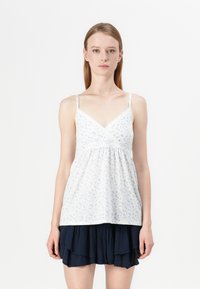 White floral tank top with blue patterns, lace trim along the neckline, and thin adjustable straps, paired with a layered navy skirt.