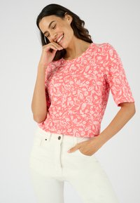 Top de manga corta con patrón floral rosa hecho de tela ligera. Cuello redondo, corte relajado, combinado con jeans blancos de cintura alta.