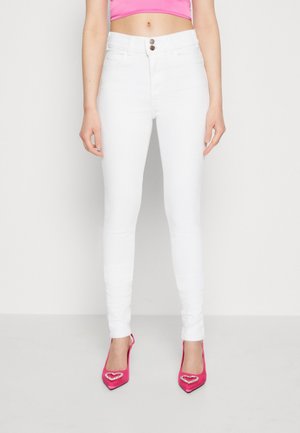 Pantalones vaqueros blancos ajustados con cintura alta y cierre de dos botones, combinados con zapatos de tacón altos de color rosa brillante que presentan acentos en forma de corazón.