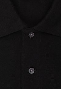 Polo nero con tessuto a maglia testurizzato, colletto a punta e due bottoni frontali con dettagli in plastica trasparente.