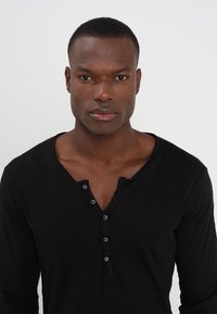 Zwarte lange mouwen henley shirt met een vierknops placket, zachte textuur en een iets ontspannen pasvorm, met een diepe V-hals.