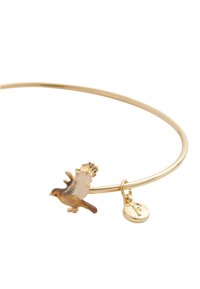 Bracelet en métal doré avec un charm oiseau détaillé et un petit pendentif portant une lettre gravée. Fini en métal lisse, design simple.