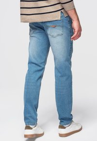 Jean en denim bleu clair à coupe droite, avec poches arrière et délavage subtil. Associé à des baskets blanches et un haut beige rayé.