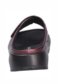 Sandale noire avec une sangle bordeaux texturée et brillante et une semelle intérieure noire rembourrée. Elle présente une semelle noire plate et robuste avec de petites rainures.