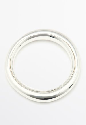 Dwa gładkie, błyszczące srebrne bransolety o nieco różnej grubości, spoczywające na białej powierzchni.