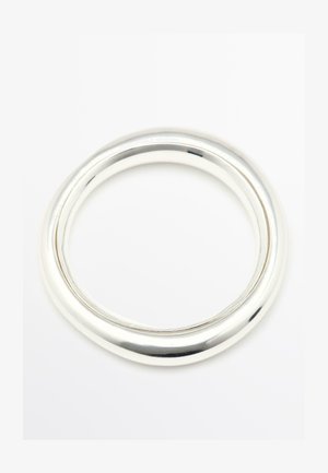 Due braccialetti rigidi lisci e lucenti in argento con spessori leggermente diversi, posati su una superficie bianca.