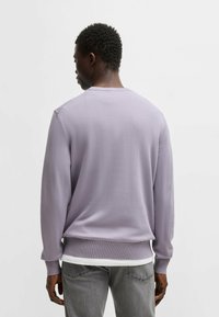 Hellblaues Crewneck-Sweatshirt aus gestricktem Stoff mit langen Ärmeln und gerippten Bundabschlüssen, kombiniert mit einem weißen Unterhemd und grauen Jeans.