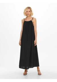 Robe maxi noire en tissu texturé avec un col froncé et des bretelles fines, descendant jusqu'aux chevilles, associée à des sandales à lanières.